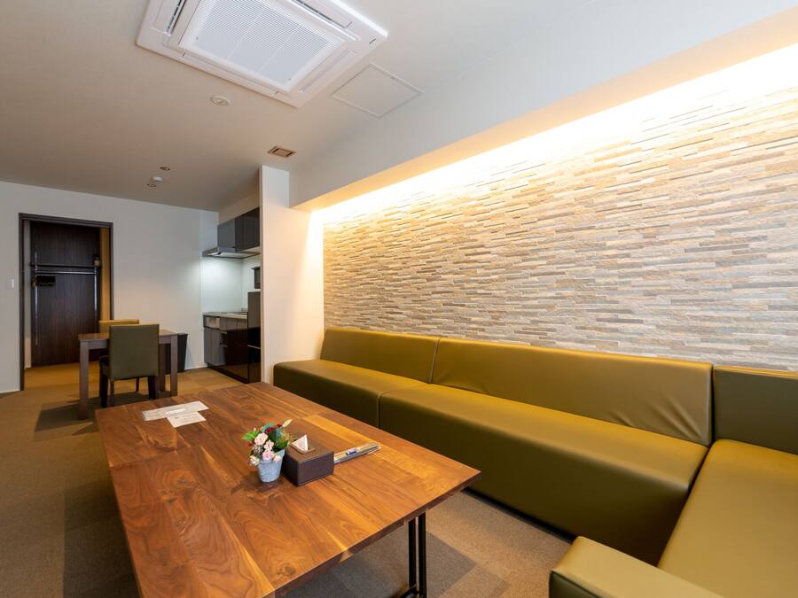 A modern living room with a wooden coffee table, a green sofa, and a kitchen in the background.