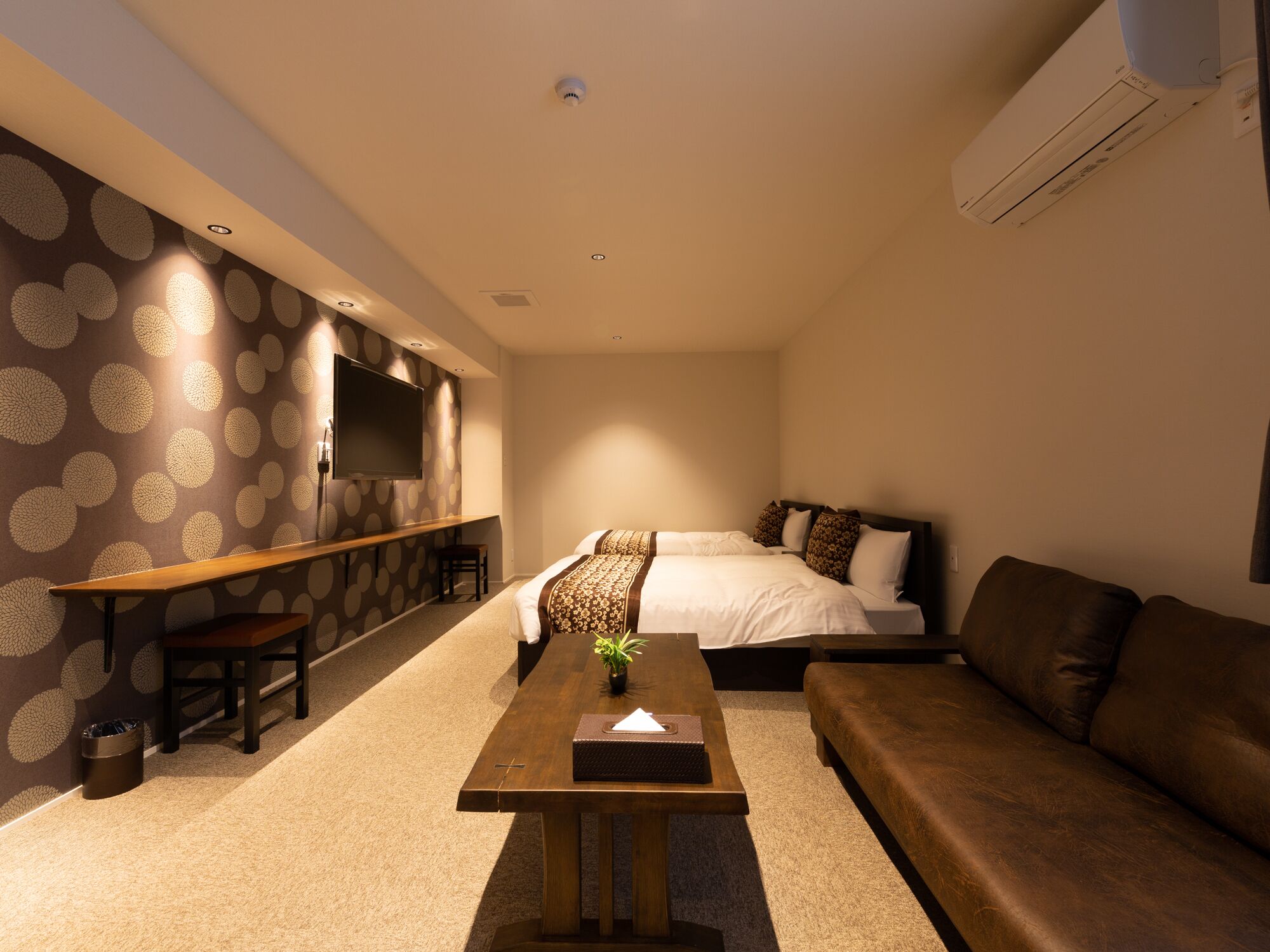 A modern hotel room with a bed, a sofa, a desk, and a TV mounted on the wall.