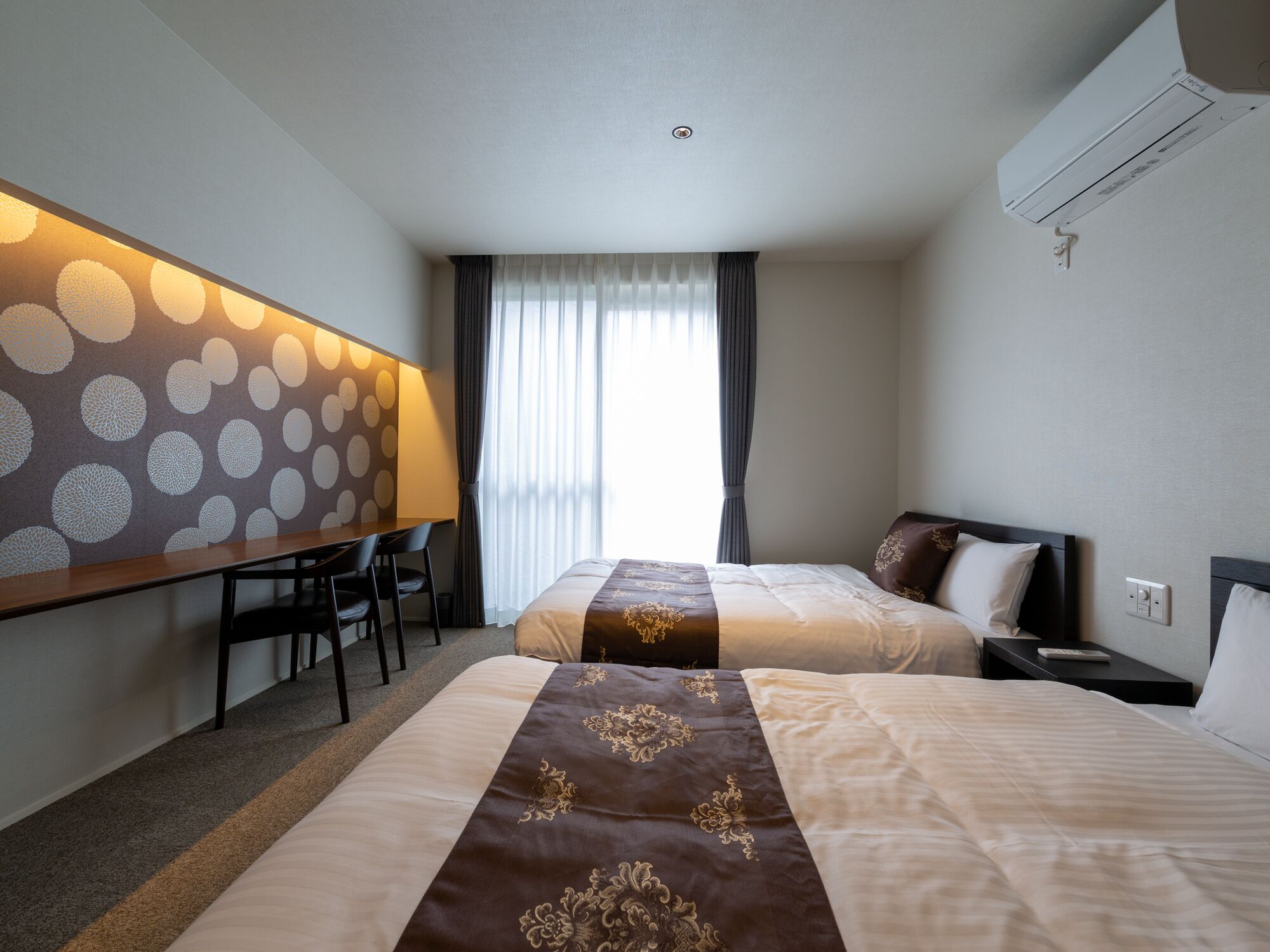 A hotel room with two beds, a desk, and a large window with curtains.
