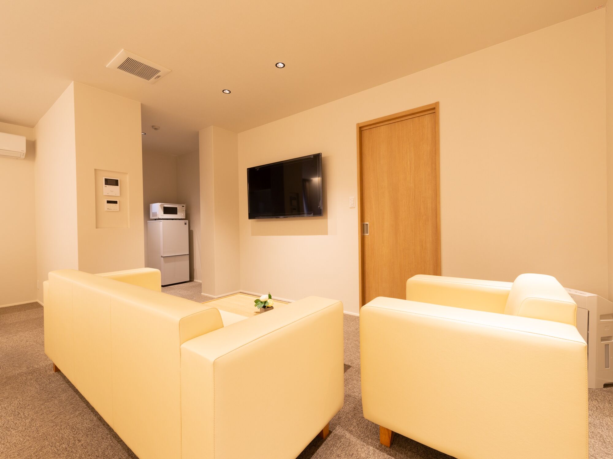 Una sala de estar con dos sofás de color crema, un televisor de pantalla plana montado en la pared y una puerta de madera.