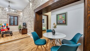 A room with a stone wall, wooden ceiling, a round table with chairs, a TV, and a colorful artwork. - Apartment close to the beach and main street (Dubrovnik)