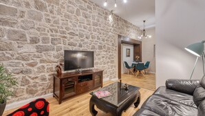 A living room with a stone wall, a wooden entertainment unit, a leather sofa, and a coffee table. - Apartment close to the beach and main street (Dubrovnik)
