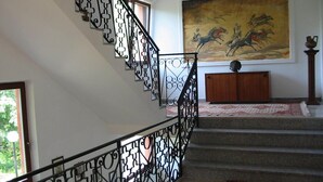 Una escalera con barandales negros decorados, un cuadro grande de caballos y un mueble de madera.