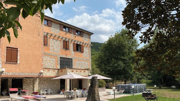 Un patio con mobiliario exterior, una fuente de piedra y un edificio con fachada de piedra y estuco.