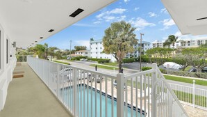 A balcony with a view of a swimming pool, palm trees, and a building in the background. - Boutique Hotel King room w/ POOL, LOCATION! Walk to BEACH/Restaurants/Nightlife (Deerfield Beach)