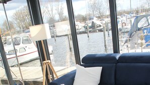 A modern living room with a blue sofa, white table, and a view of a marina through large windows.