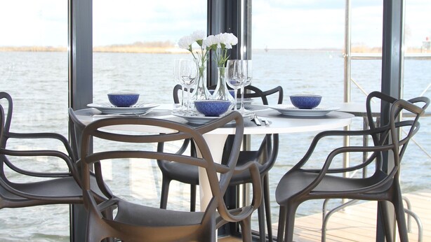 A dining table with chairs and a view of the water through large windows.