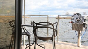 A deck with metal chairs and a table, overlooking a body of water with a distant shoreline and cloudy sky.
