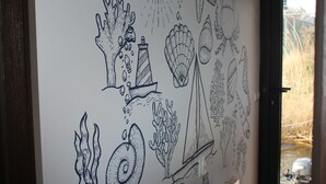 A wall with various black and white drawings of sea creatures and objects, including a lighthouse, a ship, and a sun.
