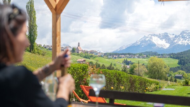 A person dining at an outdoor table with a view of a mountainous landscape and a church. - House Oberzöhr App 2 (Deutschnofen)