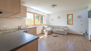 A modern kitchen with a built-in oven, a sink, and a window. There is a beige sofa and a small round table in the living area. - House Oberzöhr App 2 (Deutschnofen)