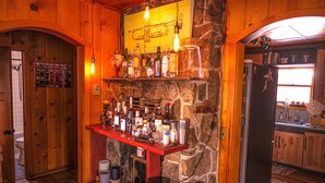 A bar area with a stone wall, wooden shelves, and various bottles. - Cozy Wilson Cabin (Wilson)