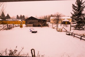 Escape to a serene winter wonderland with a rustic barn and cozy cabin, surrounded by trees and a picturesque fence.