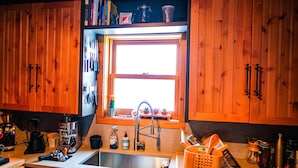 A kitchen with wooden cabinets, a window, a coffee maker, and various kitchen utensils. - Cozy Wilson Cabin (Wilson)