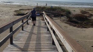 Une promenade en bois menant à une plage, avec un ciel nuageux.