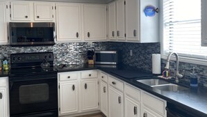 Une cuisine moderne avec des meubles blancs, une cuisinière noire, un four à micro-ondes en acier inoxydable et un plan de travail noir.