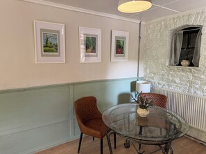 Un coin repas comprenant une table ronde en verre, deux chaises et trois tableaux représentant des paysages, accrochés au mur.