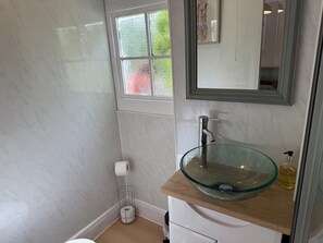 Une salle de bain avec un lavabo en verre, un porte-rouleau de papier toilette, un miroir et une fenêtre donnant sur un paysage verdoyant.