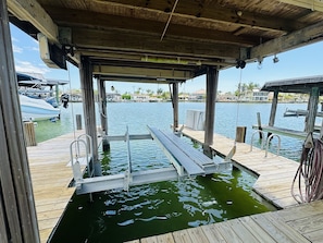 Un muelle de madera con una escalera metálica que desciende hacia el agua, rodeado por un cielo despejado y edificios al fondo.