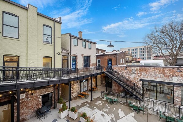 A courtyard with outdoor seating, a brick wall, and a staircase leading to an upper level.