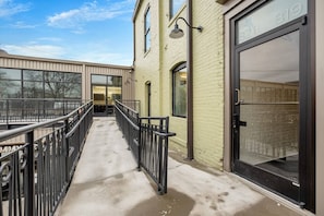 A covered outdoor corridor with metal railings, a concrete floor, and large windows on the left side.