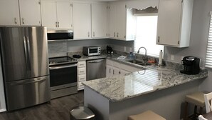 Een moderne keuken met witte kastjes, roestvrijstalen apparatuur, een granieten aanrechtblad en een inbouw kookeiland met barkrukken.