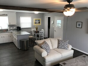 A modern kitchen with white cabinets, a dining area with a table and chairs, a beige sofa with patterned cushions, and a ceiling fan. - Newly renovated in 2021 beach house! (Carolina Beach)