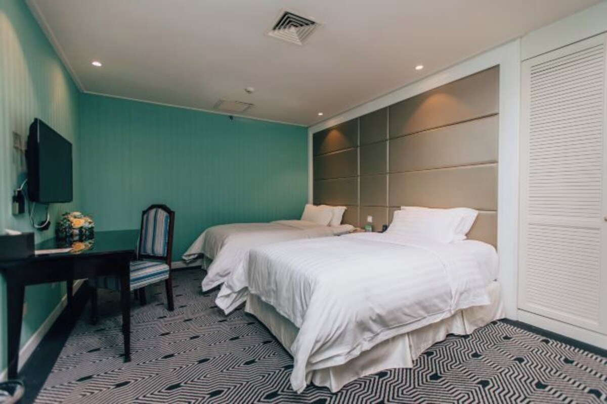 Habitación de hotel con dos camas, un escritorio, una silla y un televisor.