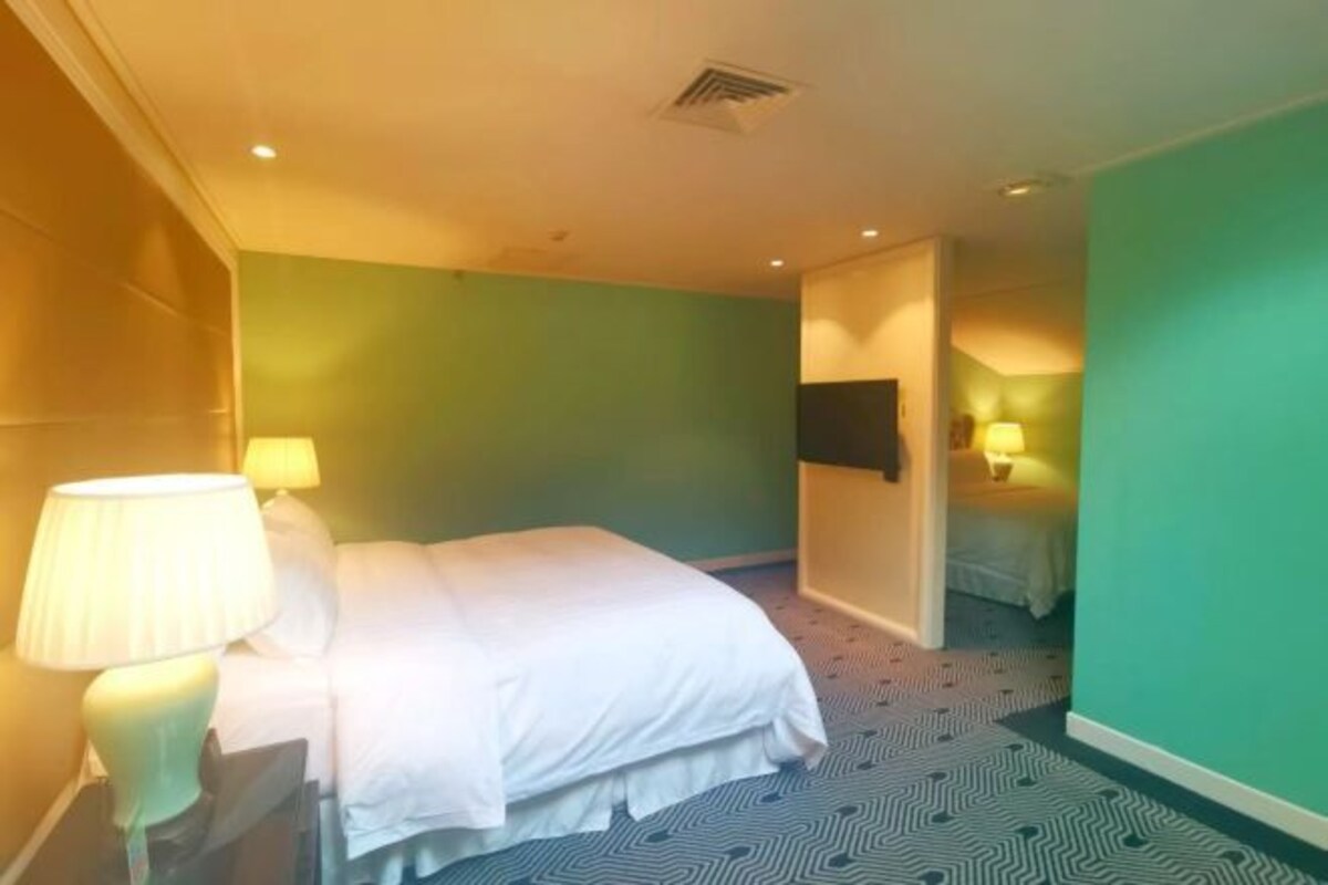 A hotel room with a bed, two bedside lamps, a wall-mounted TV, and a patterned carpet.