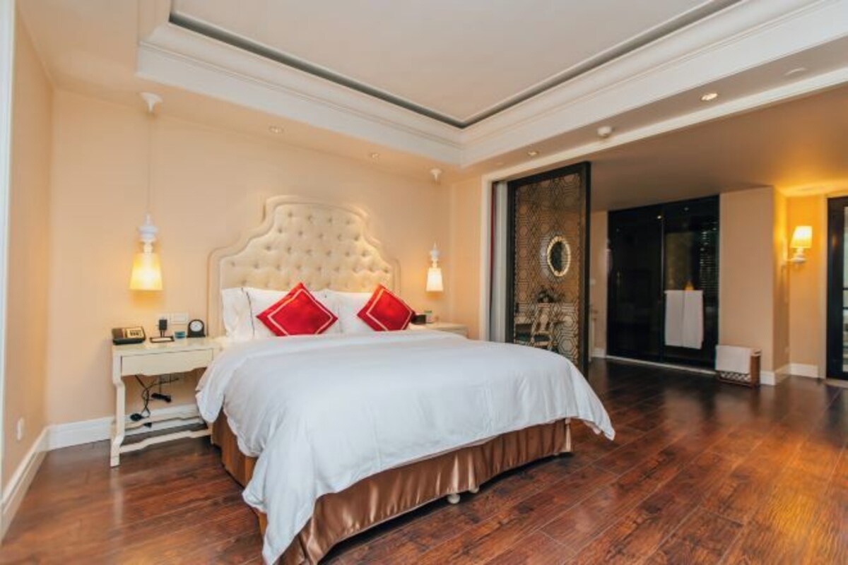 Una habitación de hotel con una cama grande, una mesita de noche, una lámpara de pared y vistas de la ciudad a través de una puerta de vidrio.