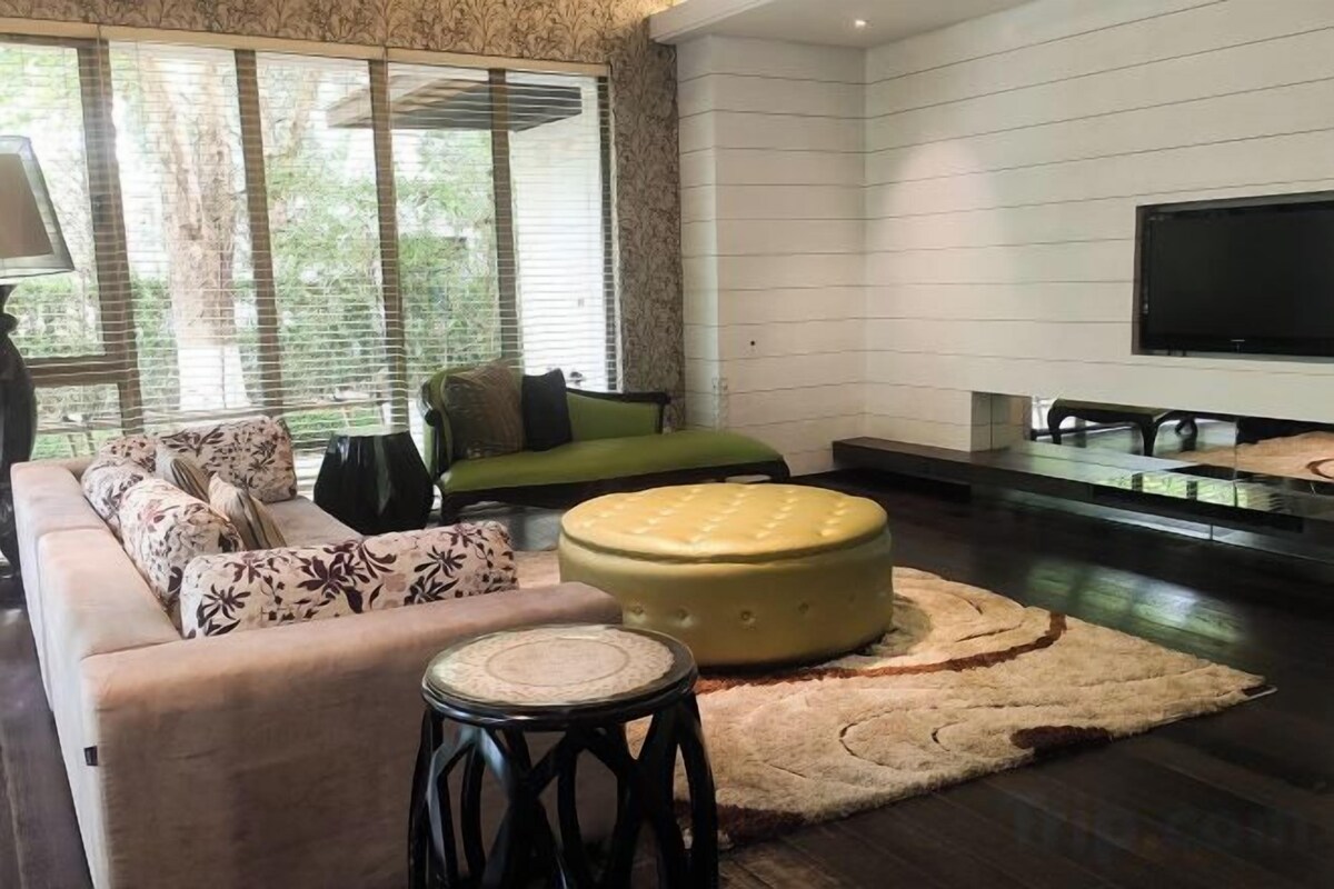 A modern living room with a sofa, ottoman, and a flat-screen TV.