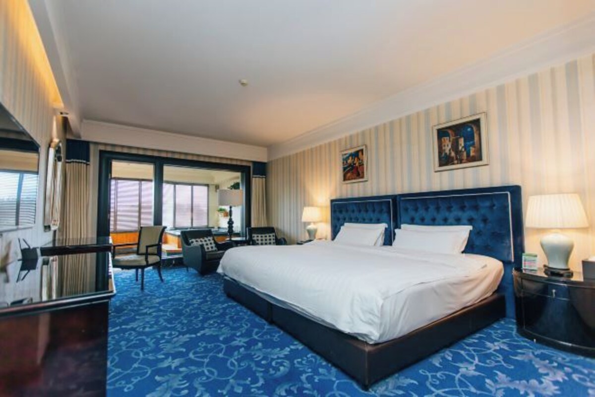 Habitación de hotel con una cama grande, un escritorio con silla, un teléfono y una ventana con cortinas.