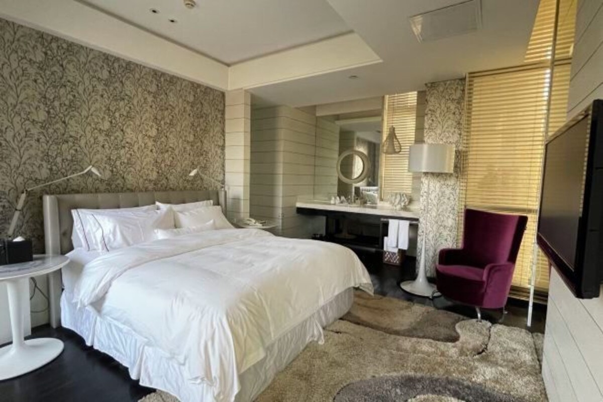 Una habitación de hotel moderna con una cama grande, un tocador con espejo, un sillón rojo y un televisor de pantalla plana.
