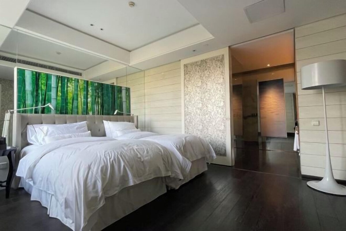 Une chambre moderne avec un grand lit, un miroir et un mur orné d’une fresque représentant une forêt verdoyante.