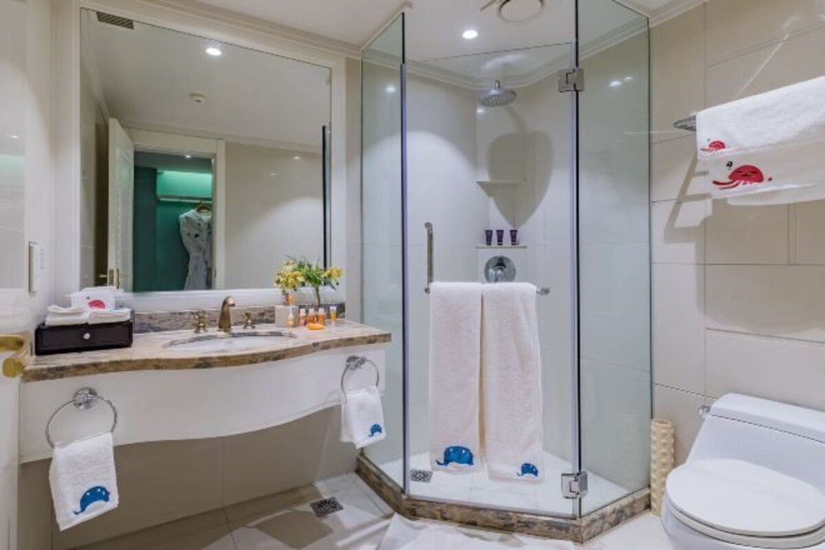 Un baño moderno con ducha envuelta en vidrio, lavamanos de mármol y un inodoro blanco.