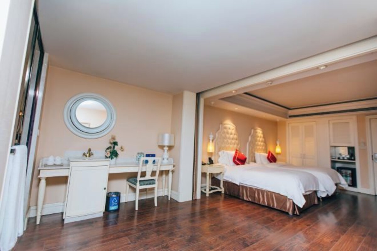 Habitación de hotel con cama, escritorio, silla, mesita y espejo redondo.
