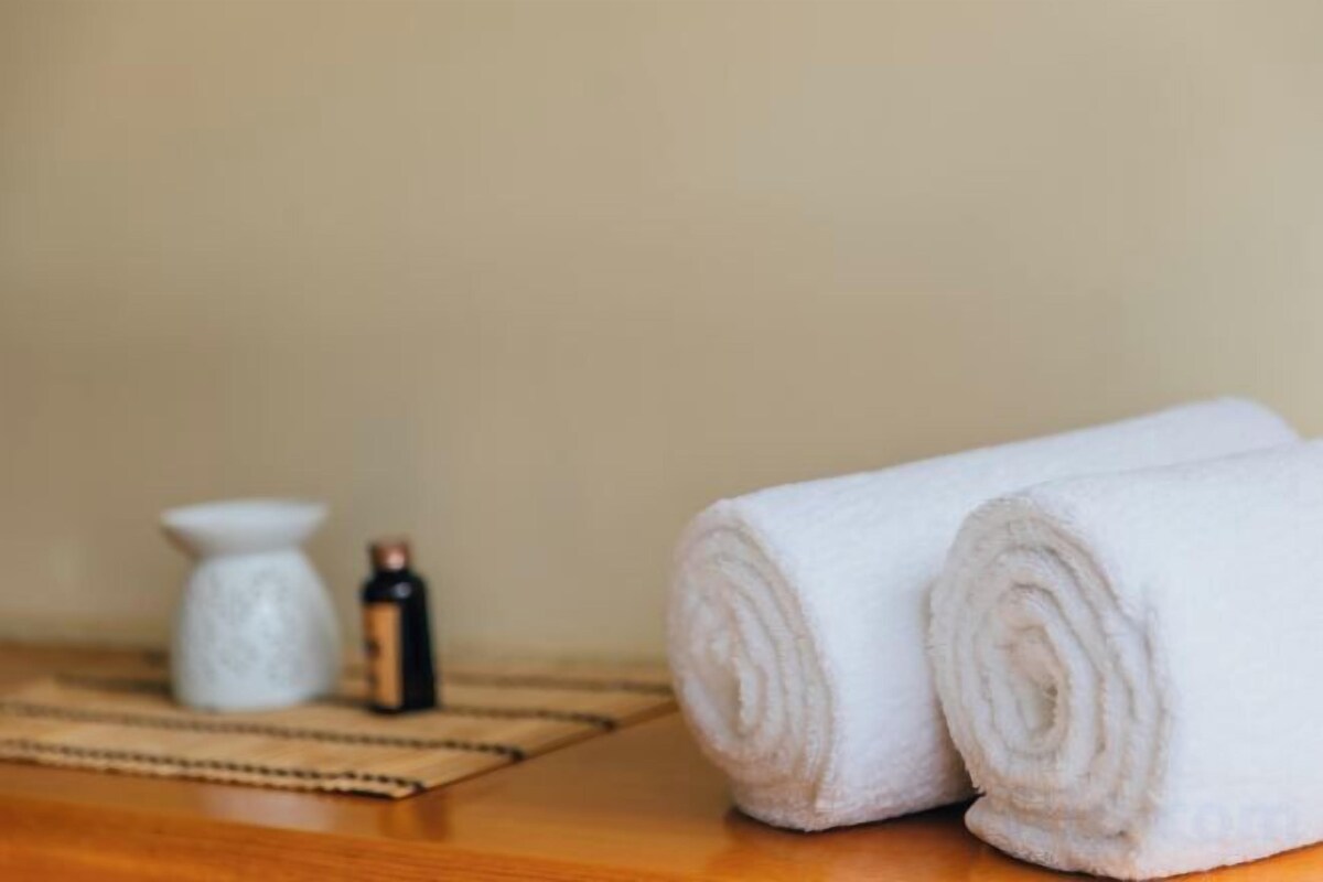 A wooden surface with two rolled white towels and a small bottle.