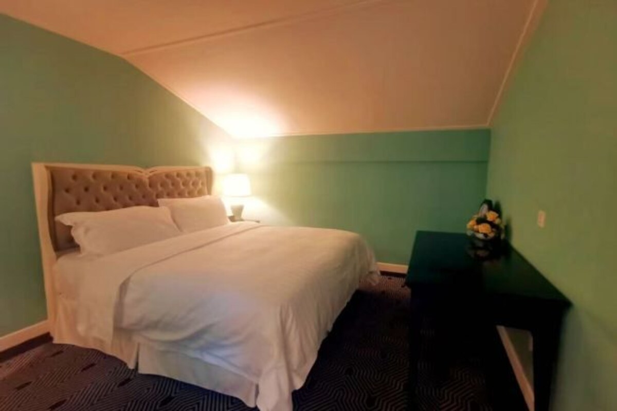 Una habitación de hotel con una cama, una mesita de noche, una lámpara y una pequeña mesa con un florero.