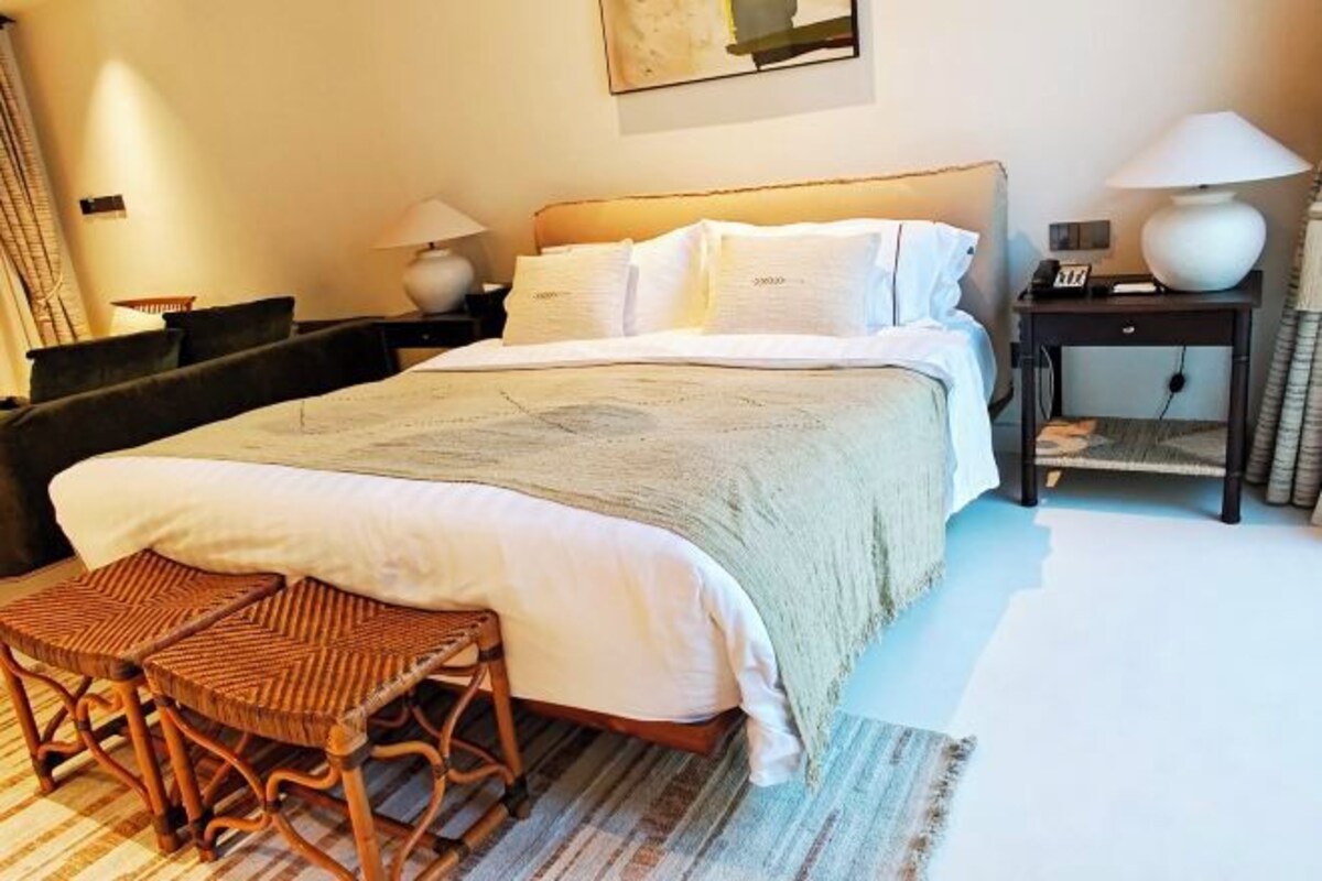 Un dormitorio ordenado con cama, mesitas de noche, lámpara, una silla y una alfombra.