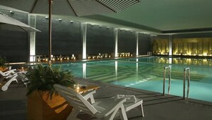 An indoor swimming pool with lounge chairs and umbrellas, surrounded by walls with vertical light fixtures. - Beijing Chunhuiyuan Hot Spring Resort Hotel (Beijing)