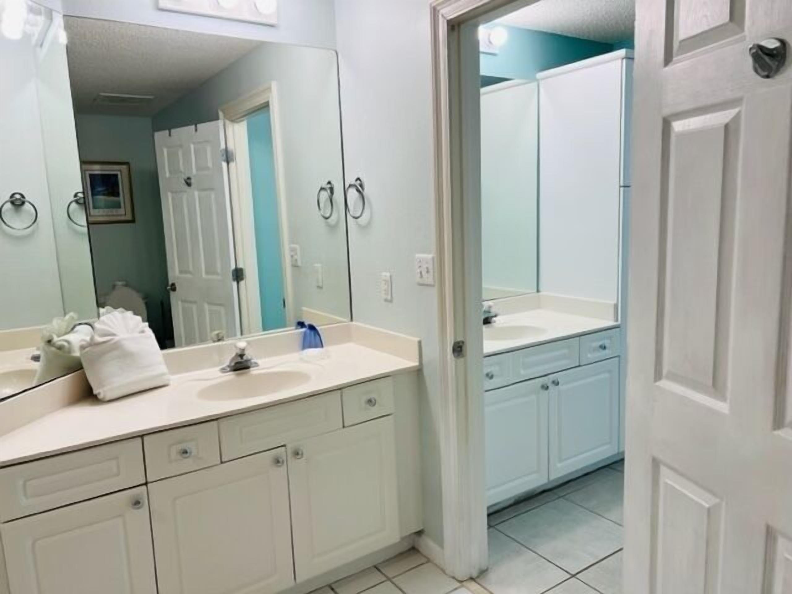Une salle de bain avec un lavabo blanc, un miroir et une porte donnant sur une autre pièce.