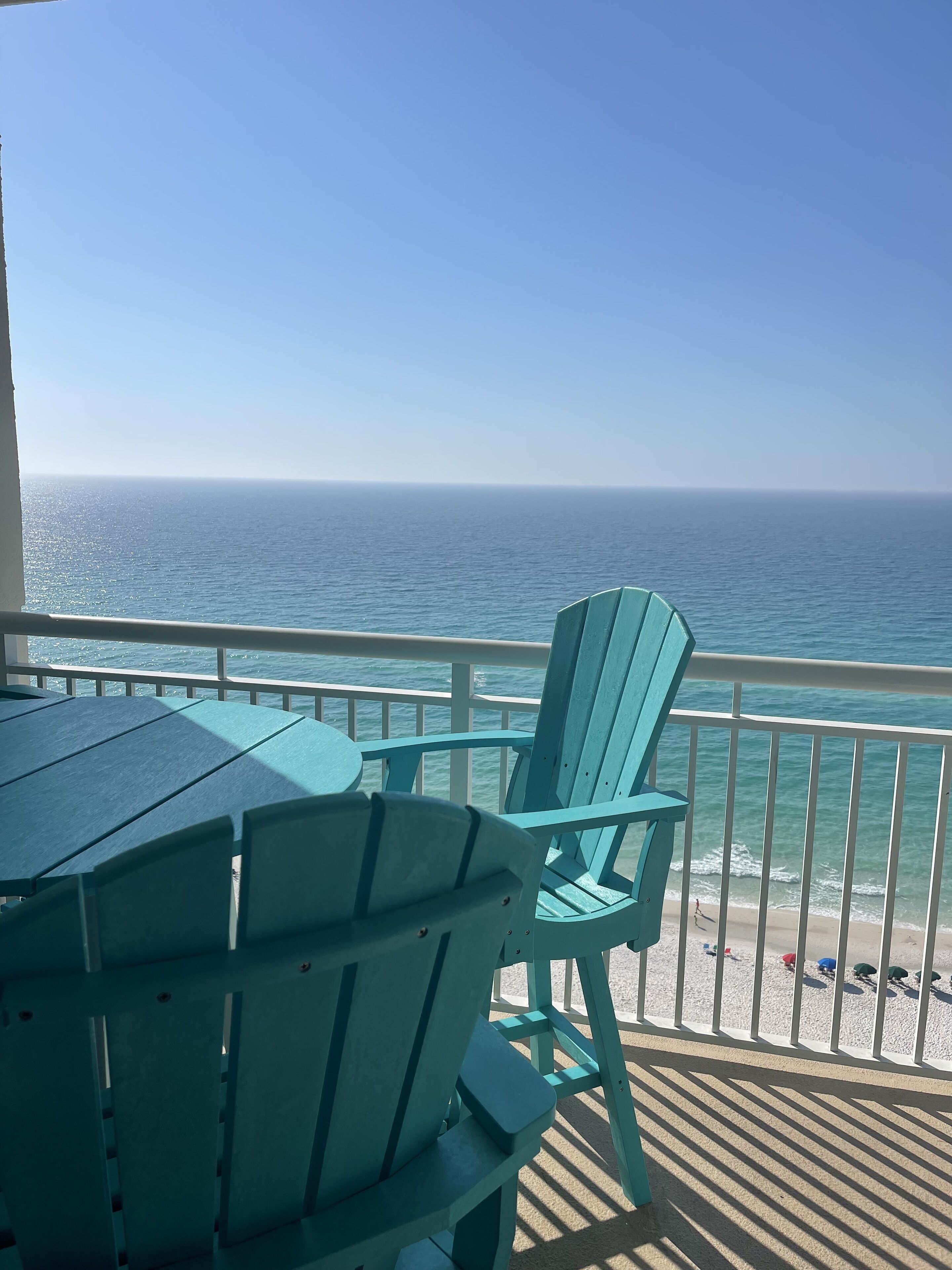 A balcony with a view of the ocean, featuring a table and two green Adirondack chairs.