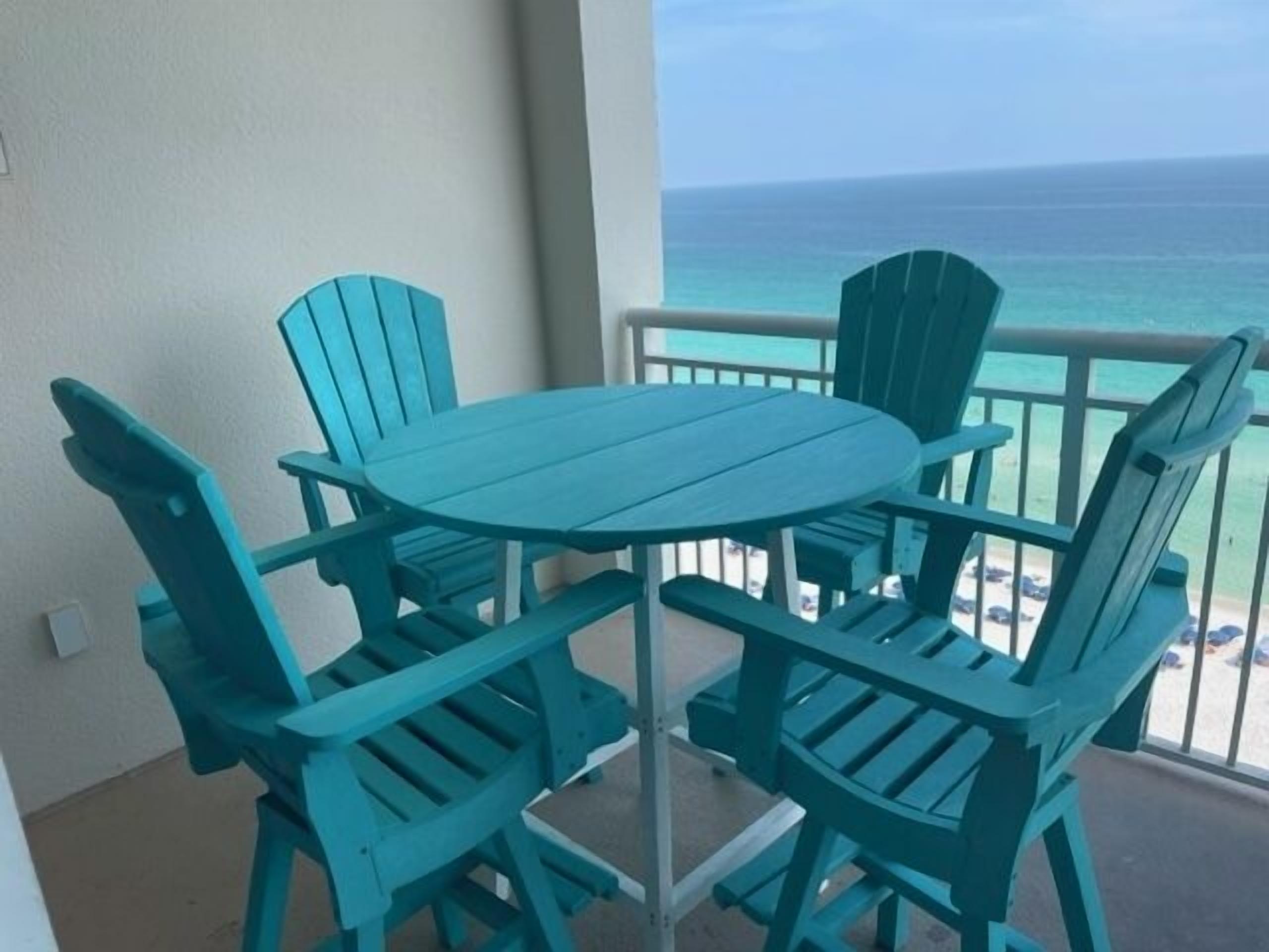 A turquoise table and four matching chairs on a balcony with a view of the ocean.