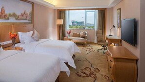 Une chambre d’hôtel avec deux lits, un bureau, une télévision et une fenêtre donnant sur un immeuble.