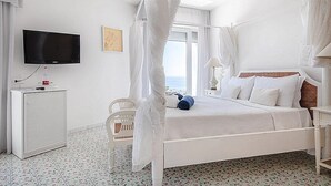 A white four-poster bed with a canopy, a television mounted on the wall, a small white cabinet, and a chair.