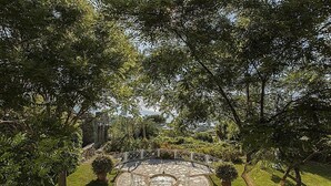 A circular stone patio with seating, surrounded by lush greenery and trees.