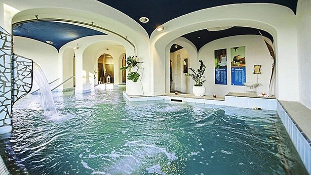 An indoor swimming pool with arched ceilings and a waterfall feature.