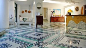 A hotel lobby with a tiled floor, a reception desk, a sofa, and a wall-mounted mirror.