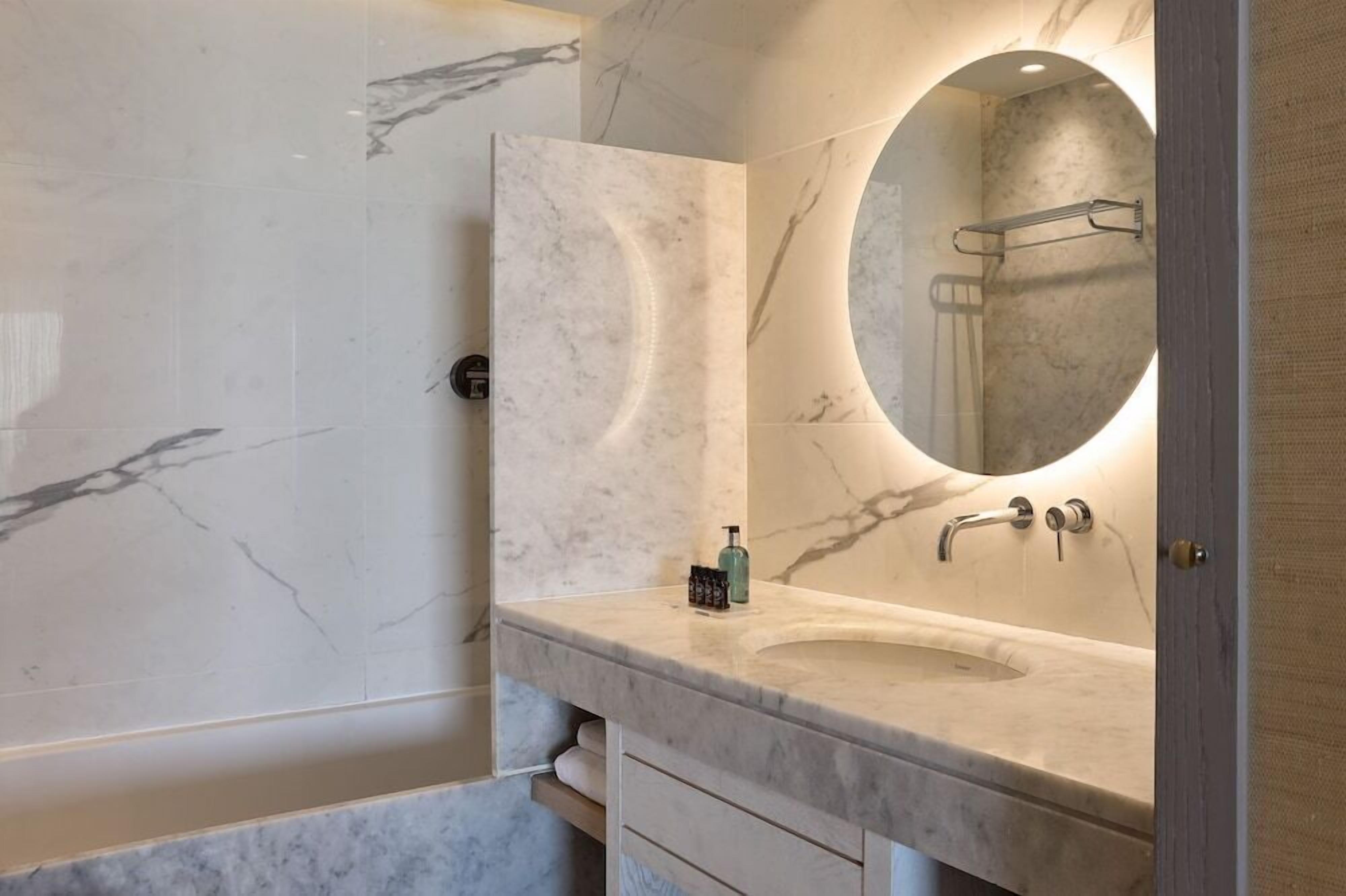 A bathroom with a marble vanity, a round mirror, and a towel rack.