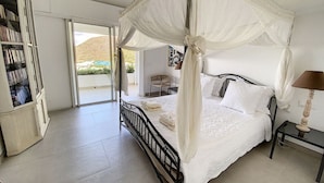 A bedroom with a four-poster bed, a bedside table with a lamp, a bookshelf, and a sliding glass door leading to a balcony. - Villa Casa Sand, luxury, 5 min walk from Anse Marcel beach (Anse Marcel)